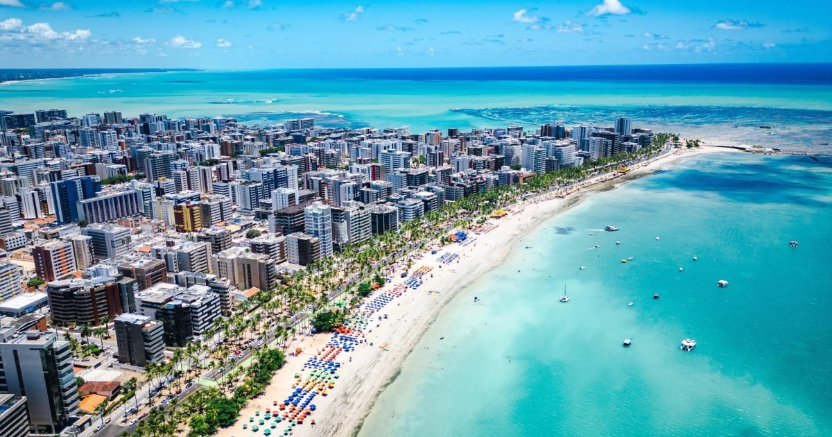 Vista aérea da orla de Maceió com mar azul e faixa de areia
